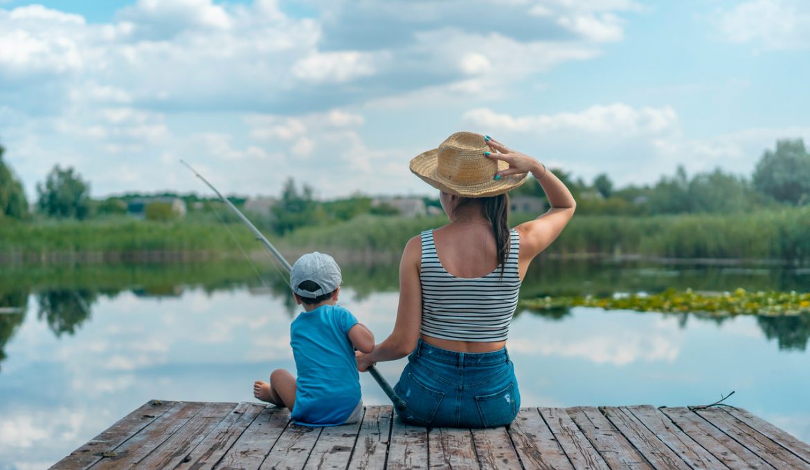 Mor og barn sidder og fisker ved sø